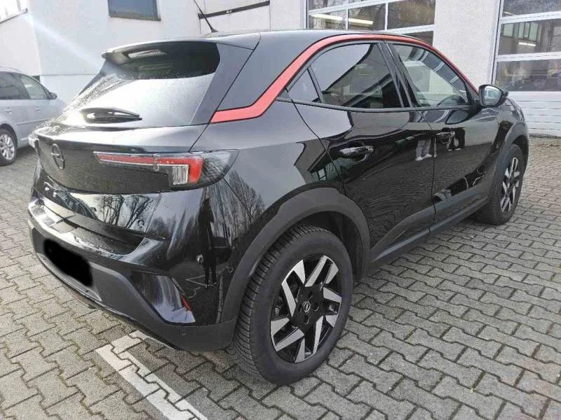 Carro preto compacto estacionado em pátio com piso de tijolos, vista traseira e lateral direita.