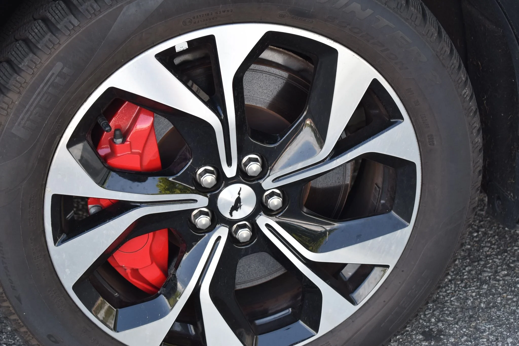 Roda de carro esportivo com design em preto e prata, calçado com pneus Bridgestone e freio de tambor vermelho visível também na roda.