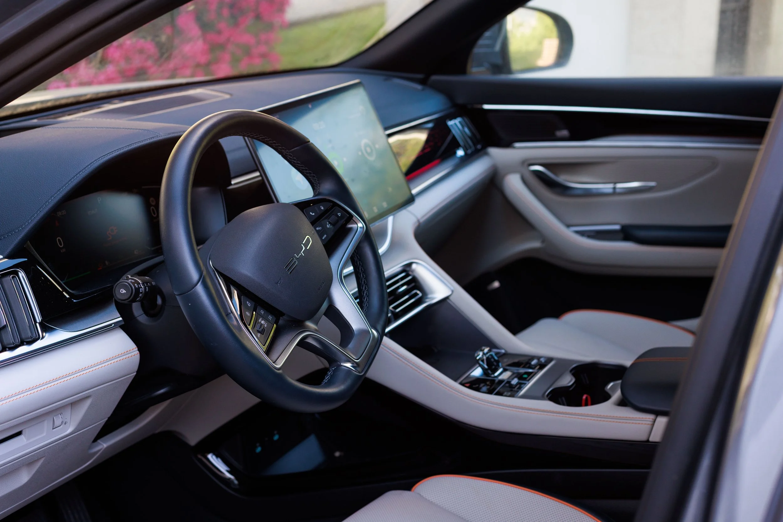 Interior de um carro com painel digital, volante com controles e assentos brancos com detalhes em laranja.
