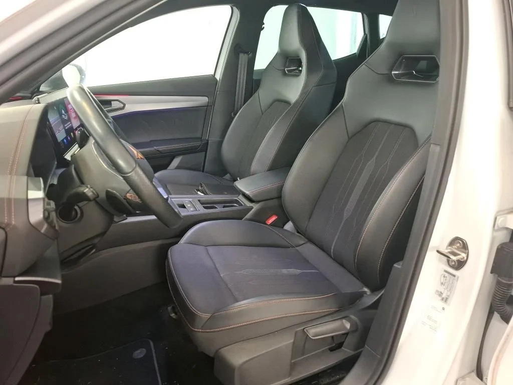 Interior de um carro, com dois assentos esportivos na frente e o painel de controle visível, incluindo o volante e o display digital.