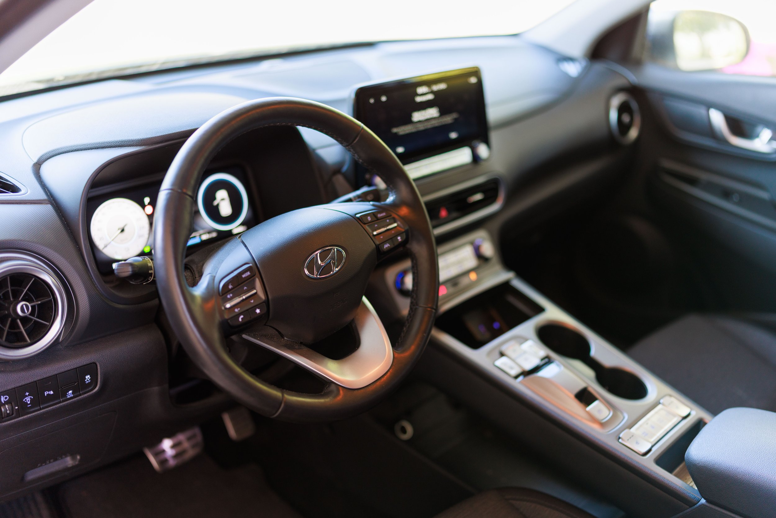 Interior de carro Hyundai, com painel digital, volante, central multimídia e controles de clima.