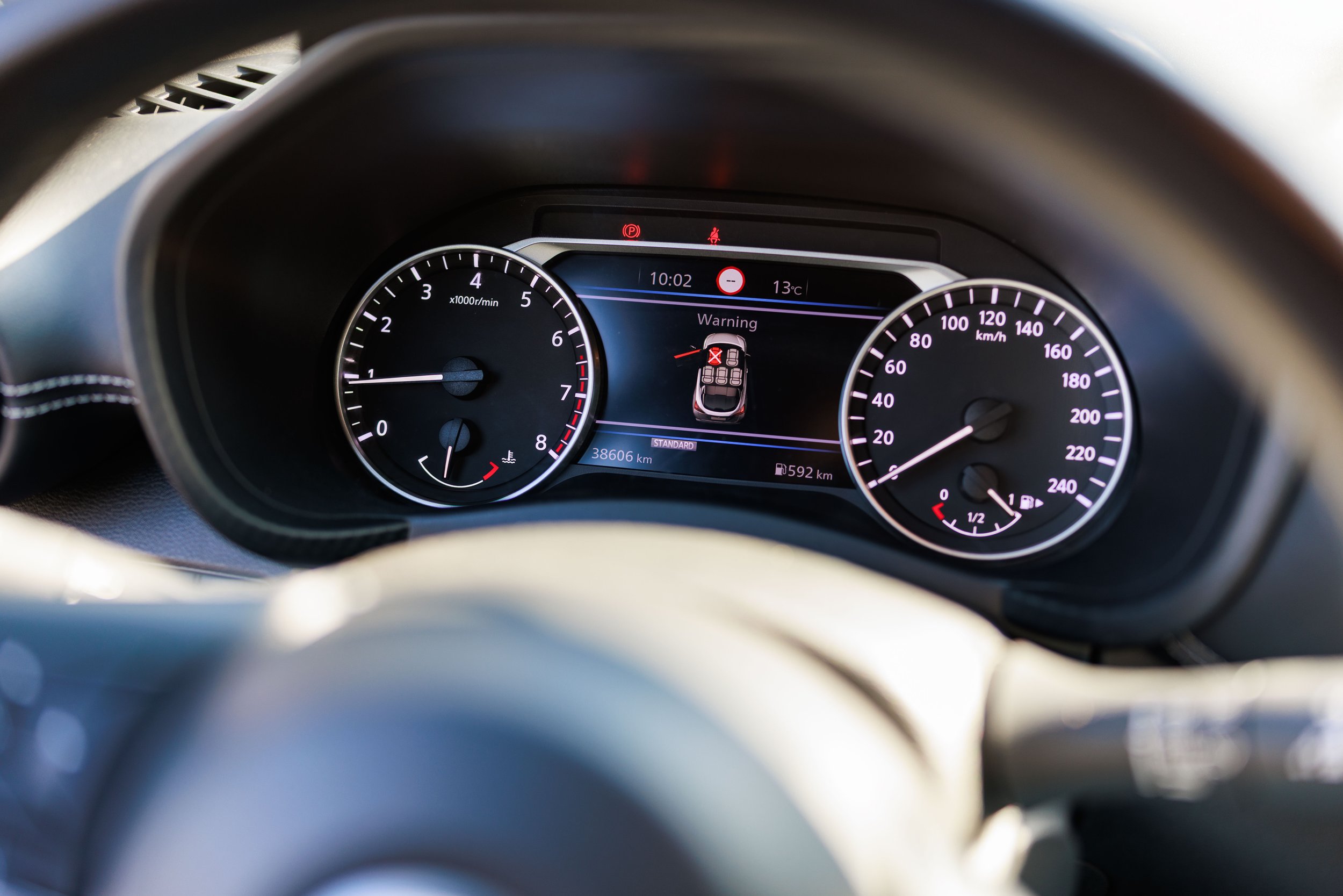 Painel de instrumentos de um carro, mostrando velocidade em km/h, RPM, nível de combustível e avisos no visor digital.