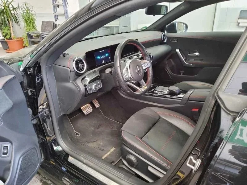 Interior de carro esportivo com banco de couro preto com detalhes vermelhos, volante de couro, painel digital e centro de controle com direção ao motorista.