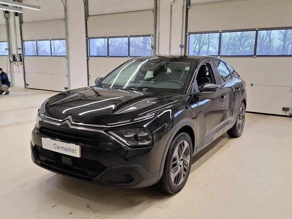 Carro preto estacionado dentro de um galpão com portas de correr e janelas de vidro.