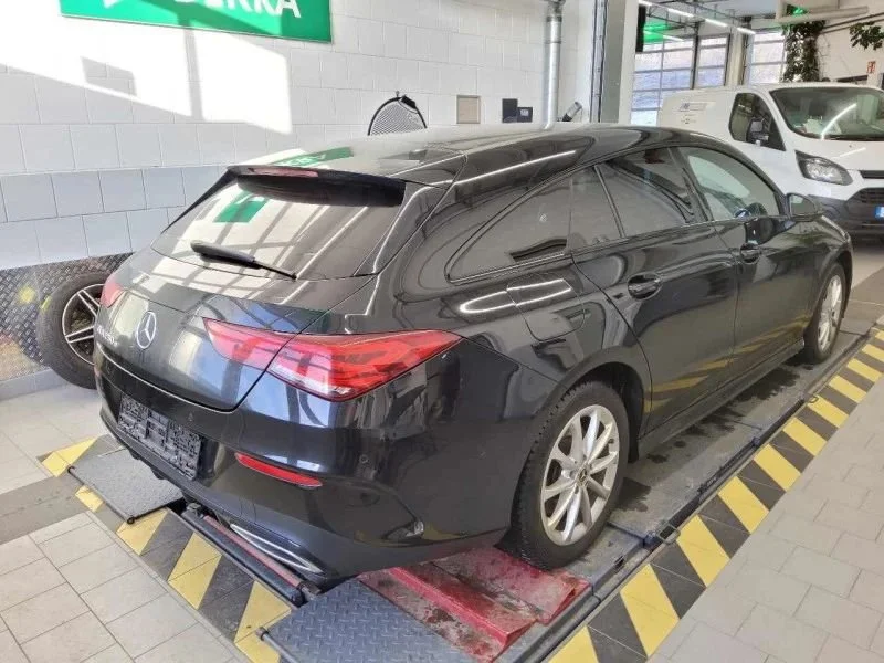 Carro Mercedes-Benz preto estacionado em uma loja, com rampas de aferição de peso na elevação. Ao fundo, há um veículo branco e uma parede branca com sinalização em verde.