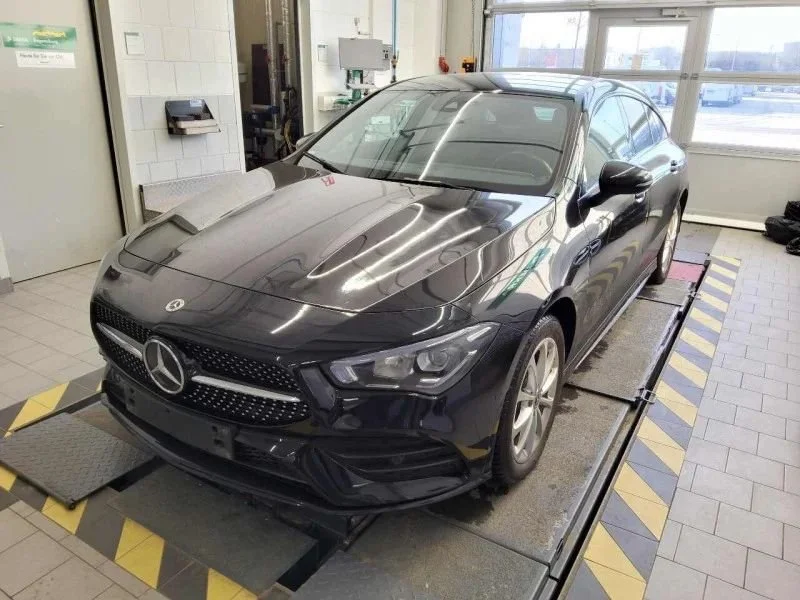 Carro Mercedes-Benz preto parado em uma plataforma de inspeção em uma oficina, com fundo de janelas e equipamentos.