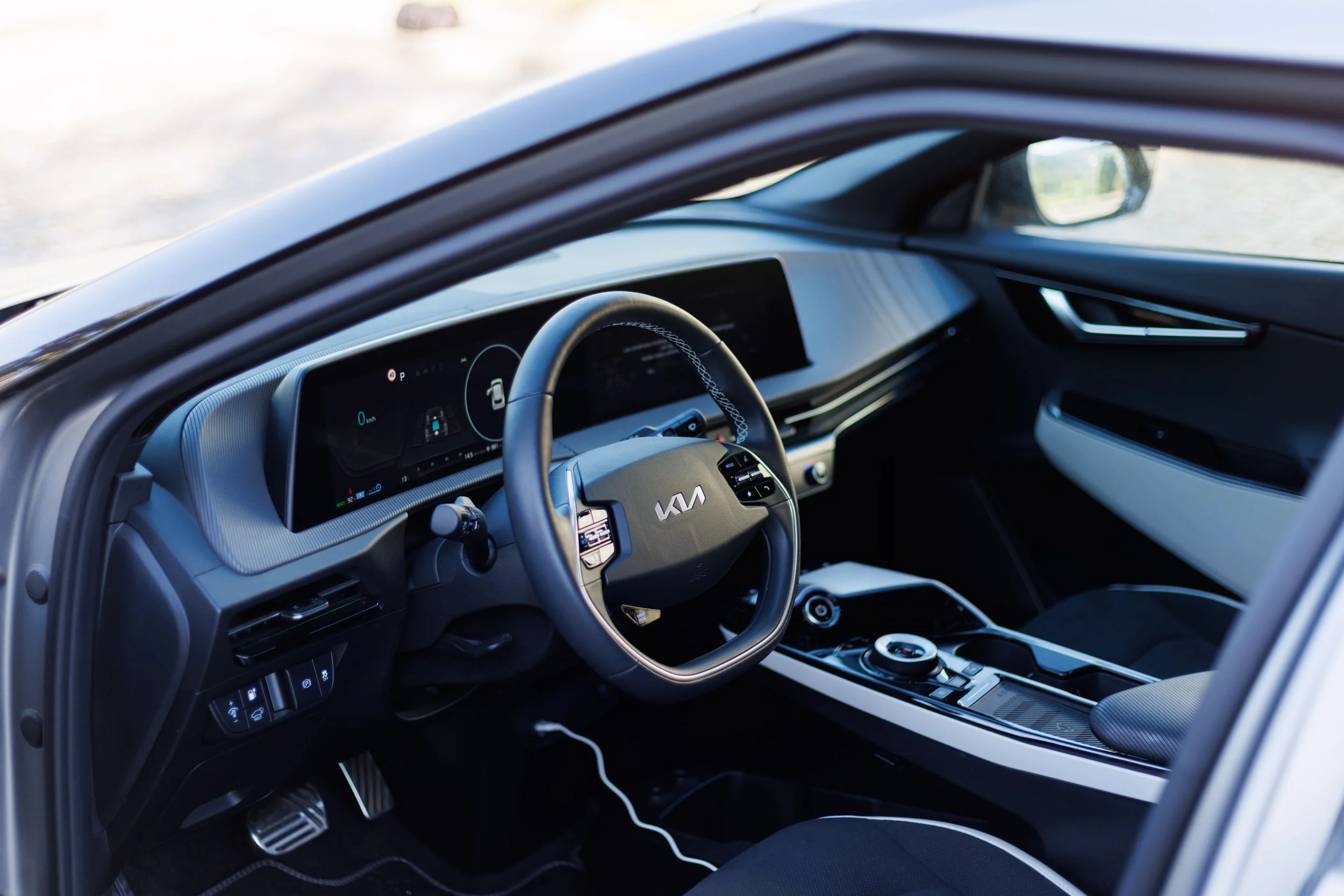 Interior de um carro elétrico Kia com volante, painel digital, câmbio e console central.