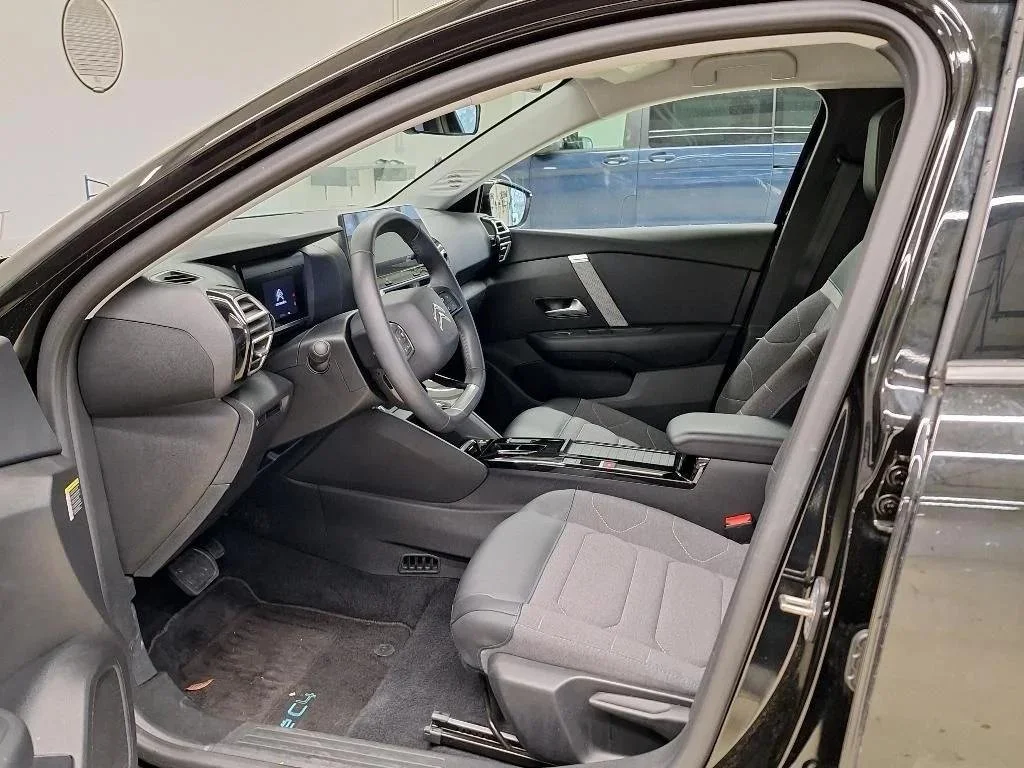 Interior de um carro moderno, com bancos de tecido cinza, painel digital e volante multifuncional, visto de lado.