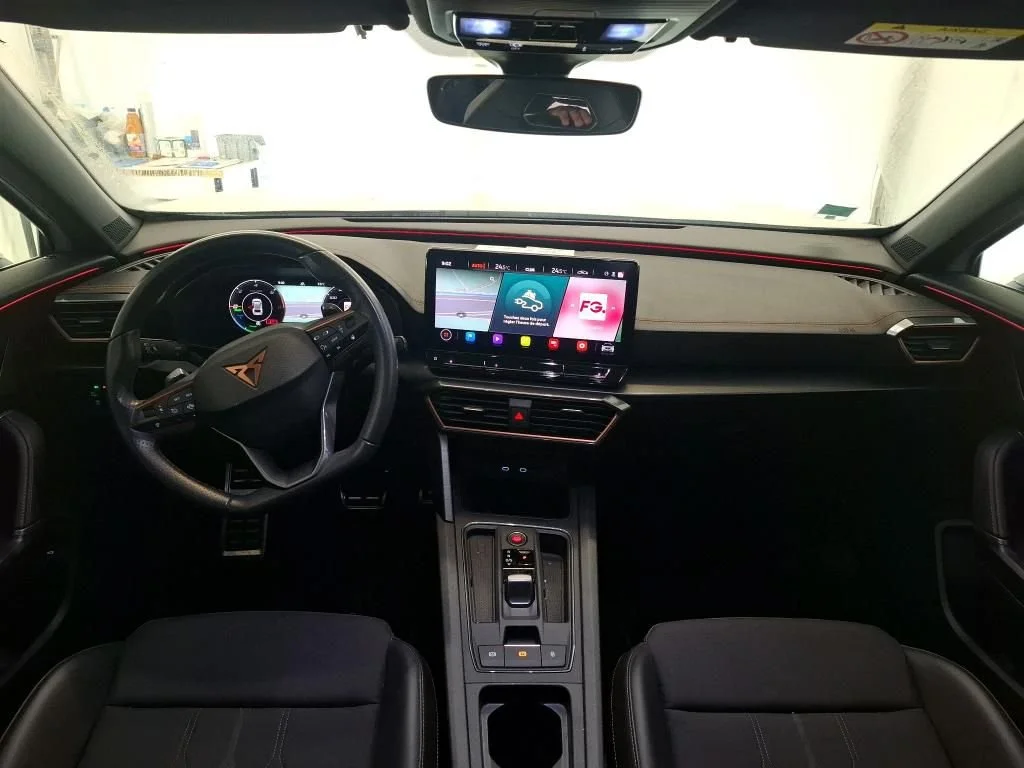 Interior de carro, foco no painel e volante, tela de entretenimento central exibindo opções de aplicativos, banco dianteiro e espelho retrovisor