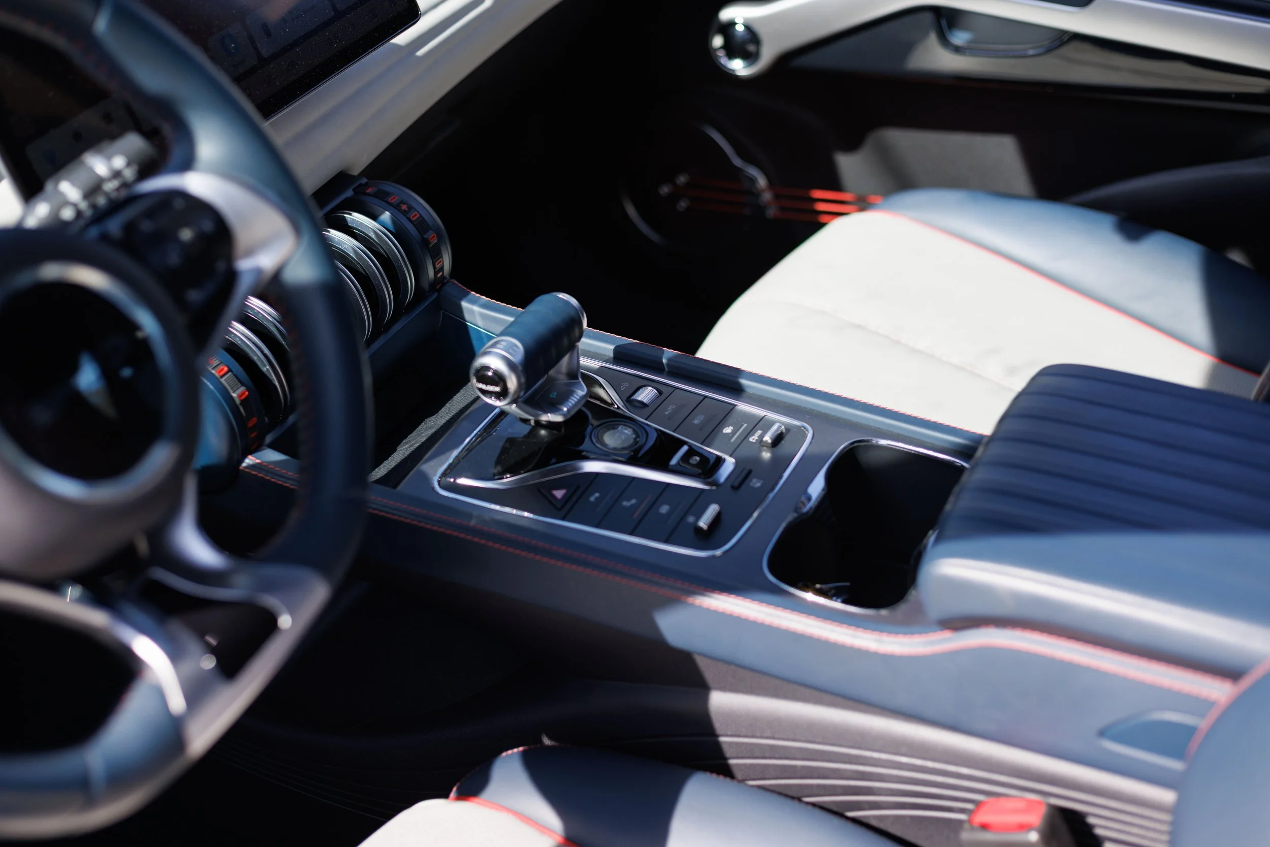 Interior de um carro de alta performance com painel digital, câmbio automático, acabamento em couro preto e detalhes vermelhos.