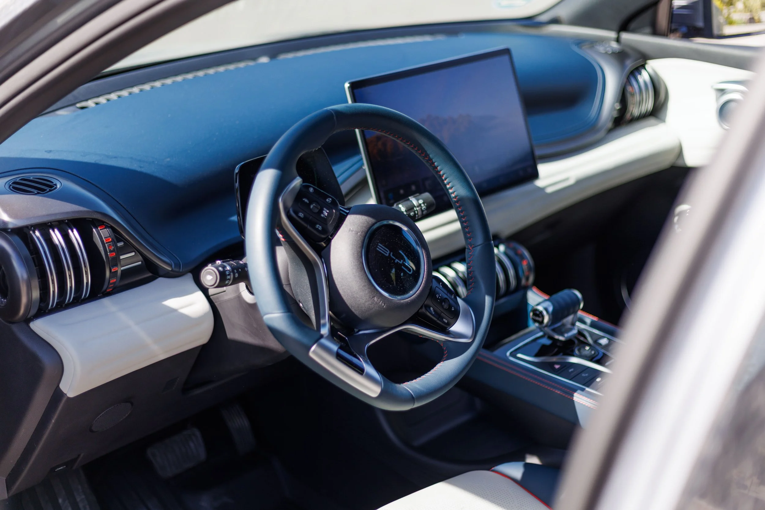 Interior de carro de luxo com volante, painel digital e detalhes em couro.