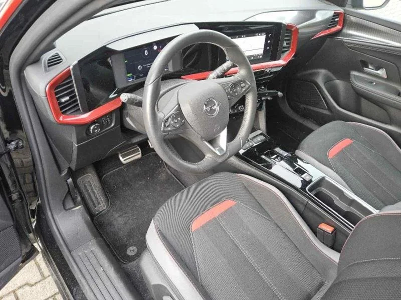 Interior de um carro, mostrando o painel, volante, banco do motorista e console central, com detalhes em preto e vermelho.