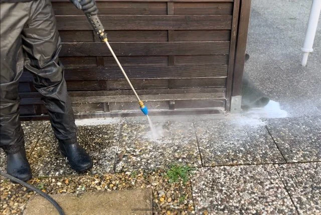 Une personne nettoie le pavé à l'aide d'un nettoyeur à haute pression.