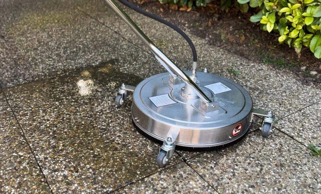 Un nettoyeur de sol industriel en action sur un pavé extérieur, avec des jets d'eau et de savon nettoyant la surface.