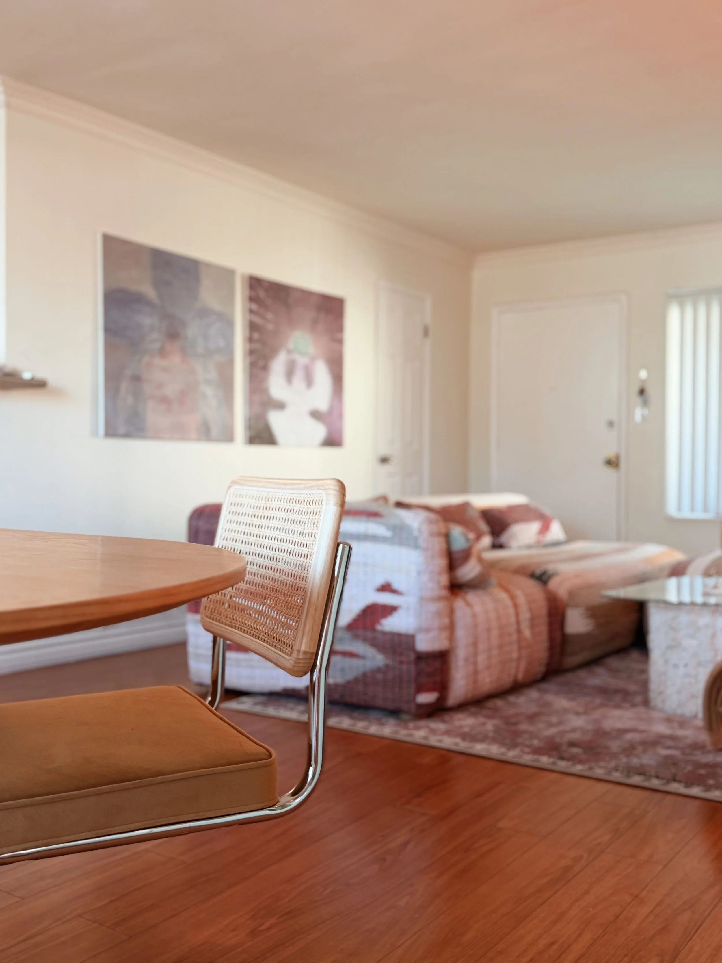 Living room with a dining table, wicker chair, patterned sofa, and framed artwork on the wall.