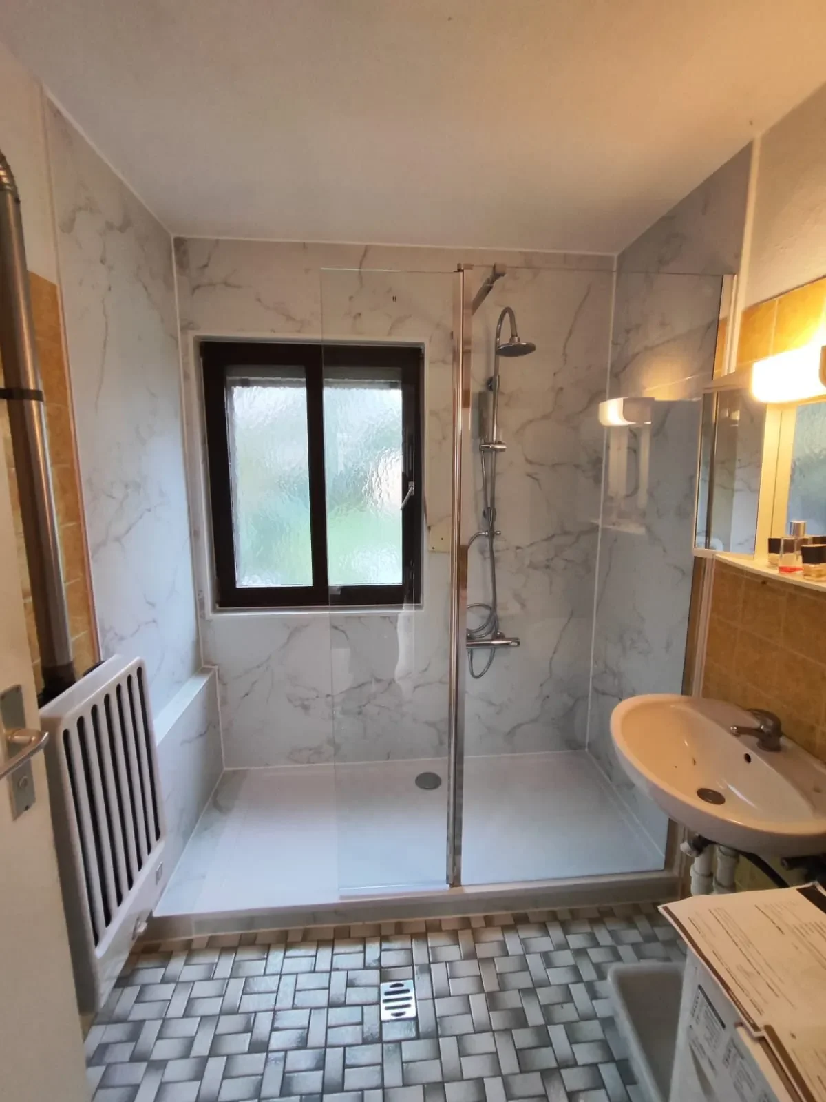 Ein Badezimmer mit einer Dusche, einem Waschbecken, einem Fenster mit frosted Glas und einer Heizung.