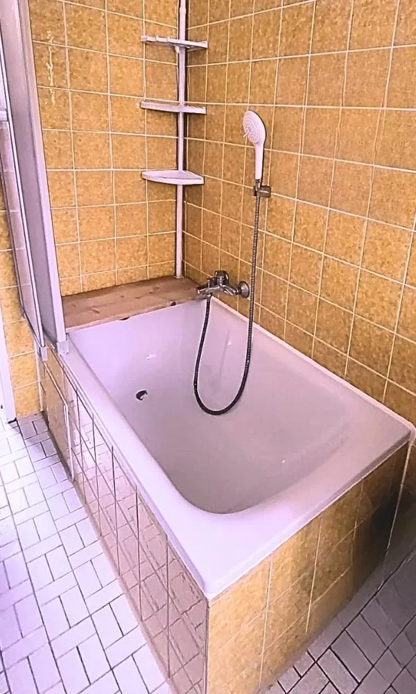 Kleines Bad mit braunen Fliesen, Badewanne mit Holzbrett und Duschkopf