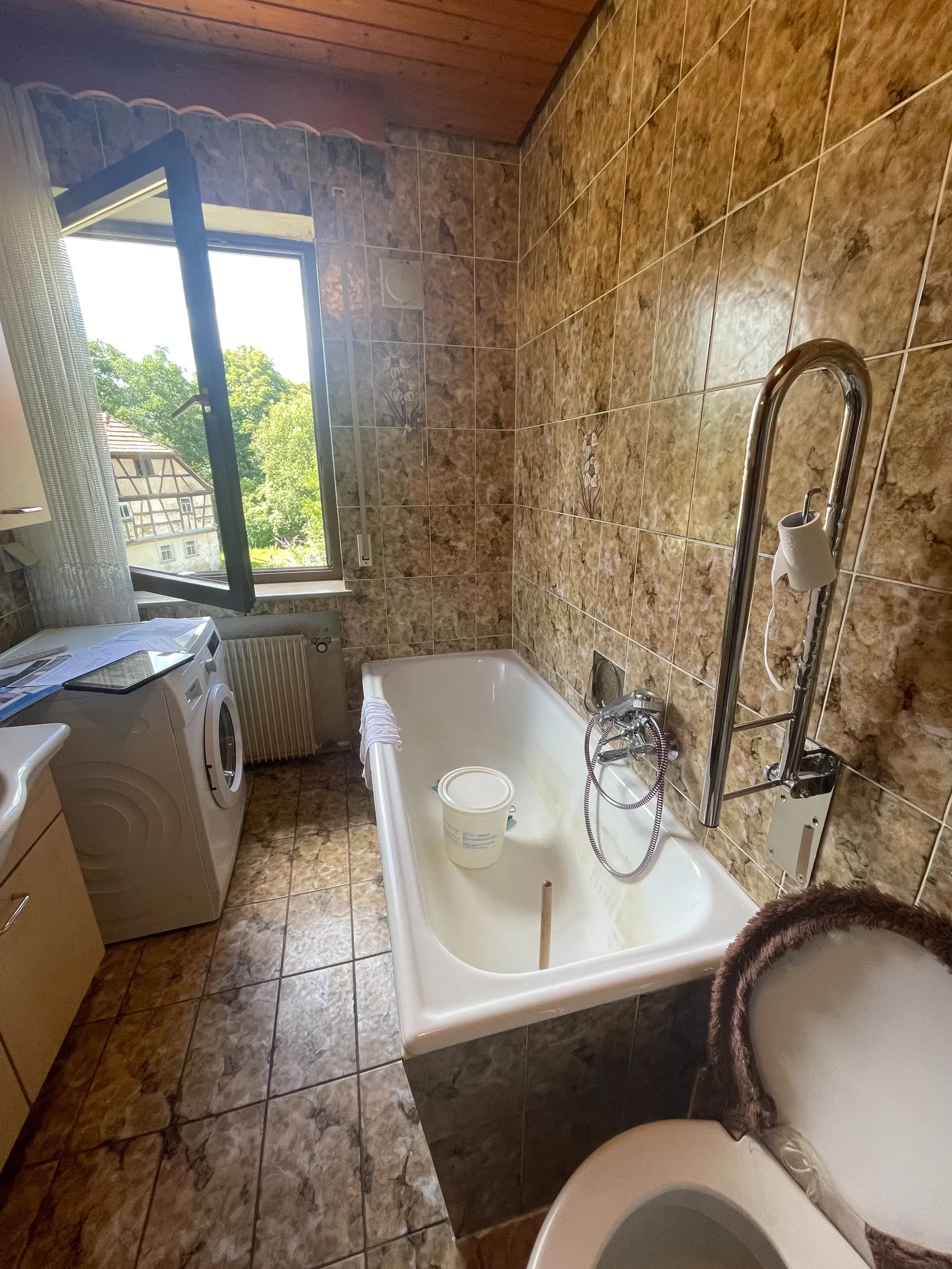 Ein Badezimmer mit Badewanne, Waschmaschine, einem Fenster und Fliesen mit Blumendekor