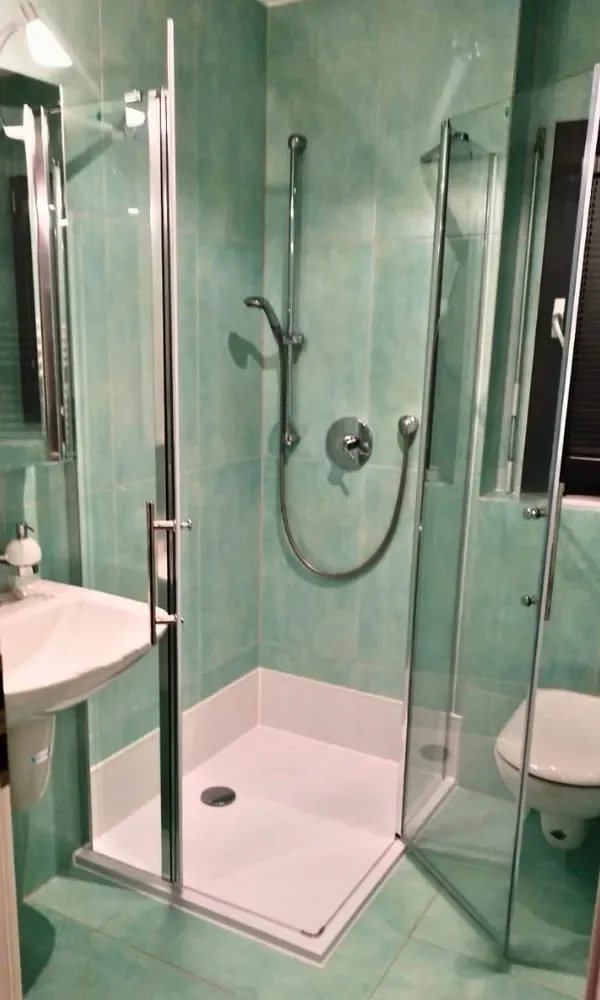 Kleines Badezimmer mit einer Dusche, Waschbecken und Toilette, alles in grünen Fliesen.