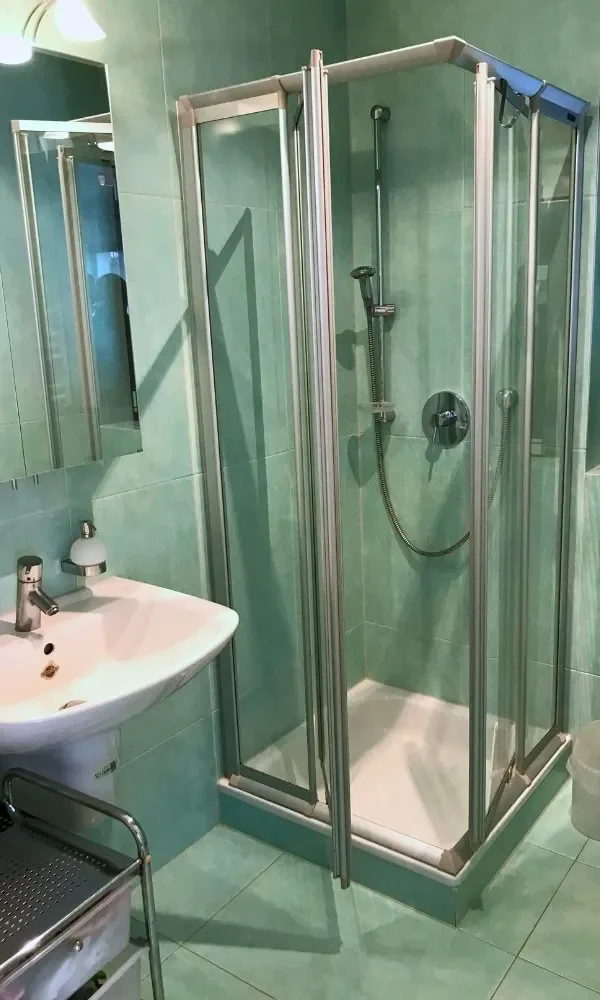 Kleines Badezimmer mit einer Eckeinstieg Dusche, weißem Waschtisch mit Armatur, Spiegel und Kleiderständer