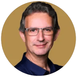 Ein Portrait eines Mannes mit dunklen Haaren, Brille und dunklem Hemd vor einem beigefarbenen Hintergrund.