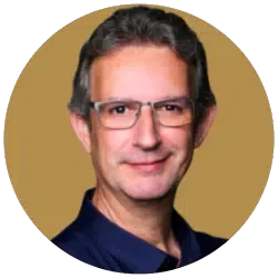 Ein Portrait eines Mannes mit dunklen Haaren, Brille und dunklem Hemd vor einem beigefarbenen Hintergrund.