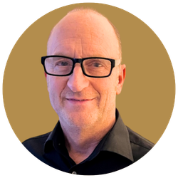 Ein kahlköpfiger Mann mit schwarzer Brille, Gesicht im Nahaufnahme, leicht grinsender Mund, goldener Hintergrund, runder Rahmen