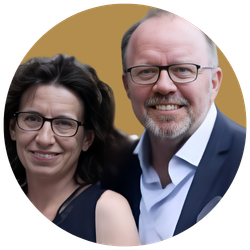 Ein Mann und eine Frau, beide lächelnd, posieren für ein Foto. Der Mann trägt eine Brille und einen Anzug, die Frau trägt eine Brille und ein dunkles Oberteil.