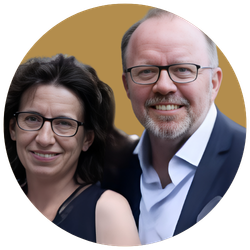 Ein Mann und eine Frau, beide lächelnd, posieren für ein Foto. Der Mann trägt eine Brille und einen Anzug, die Frau trägt eine Brille und ein dunkles Oberteil.