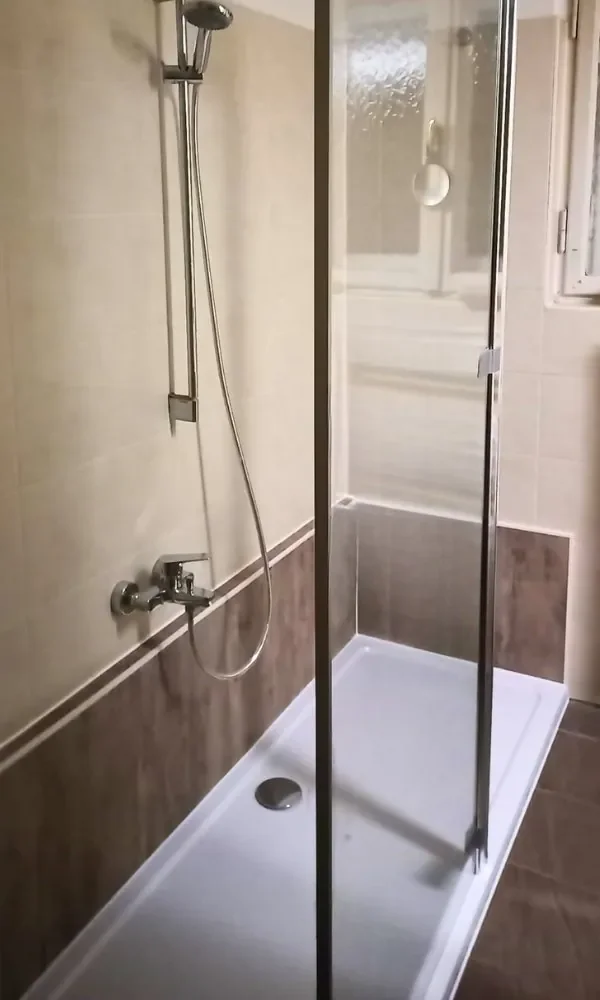 Duschkabine in einem Badezimmer mit beige- und braunfarbenen Fliesen, inklusive Duschkopf, Wasserhahn und Duschabtrennung.
