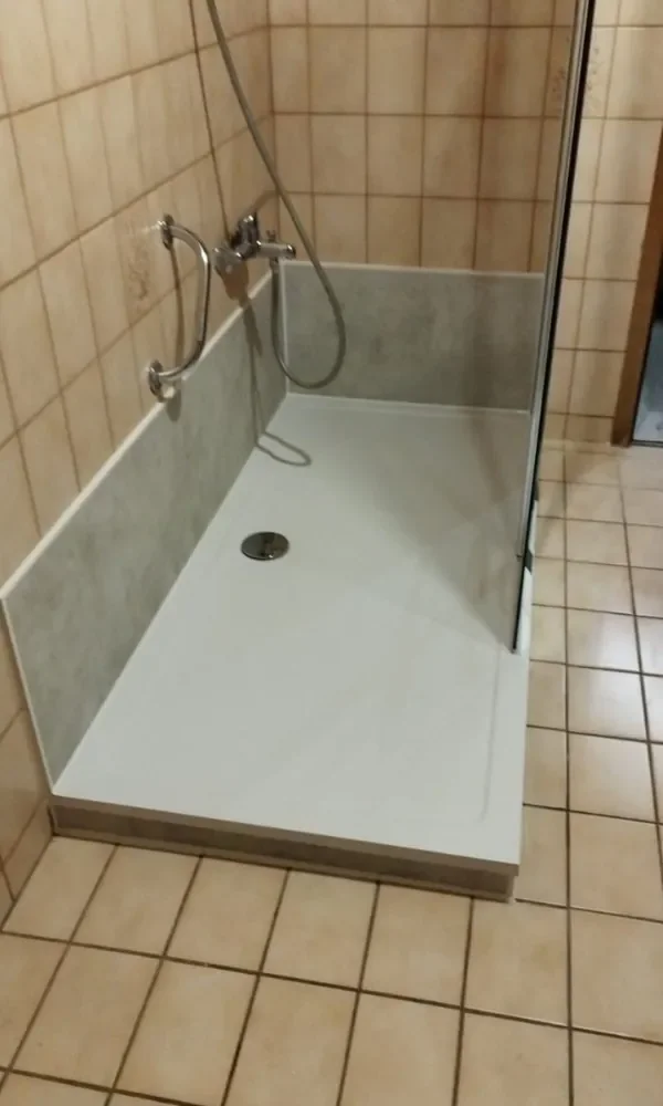 Unterboden einer offenen Dusche mit Brause und Wasserhahn, an einer Wand mit Fliesen, in einem Badezimmer.