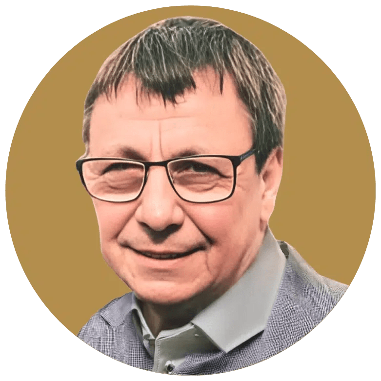 Ein Mann mit Brille und grauem Hemd lächelt in die Kamera, vor einem goldfarbenen Hintergrund.