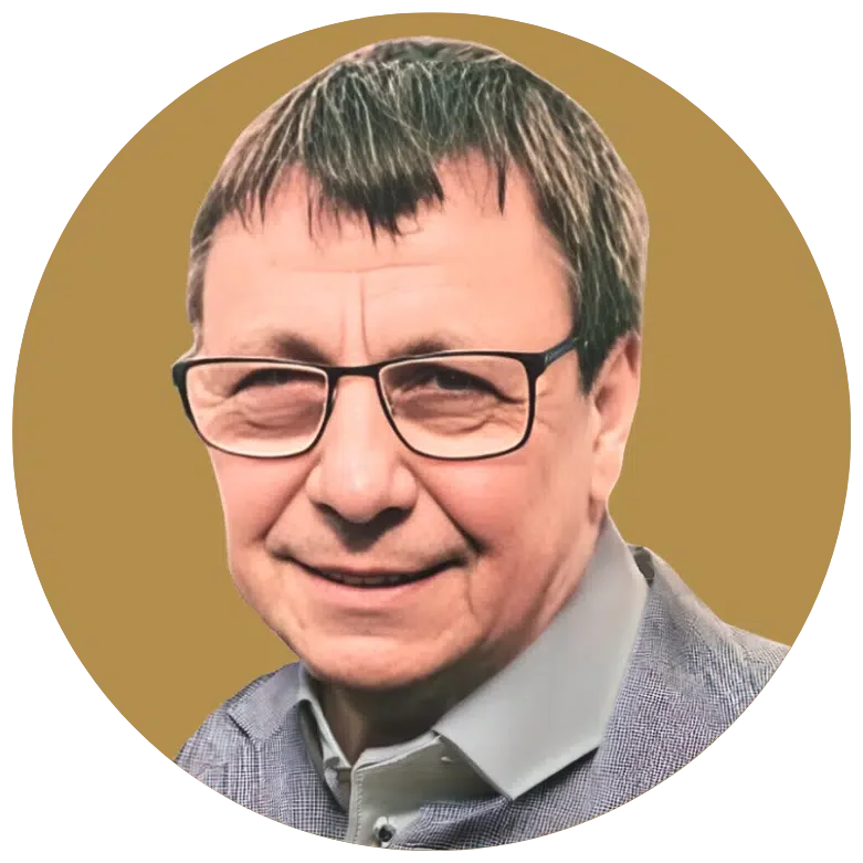 Ein Mann mit Brille und grauem Hemd lächelt in die Kamera, vor einem goldfarbenen Hintergrund.