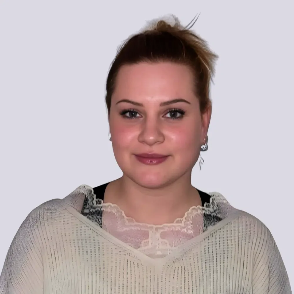 Ein Porträt einer jungen Frau mit braunem Haar, die einen schwarzen und weißen Schal trägt, vor einem hellgrauen Hintergrund.