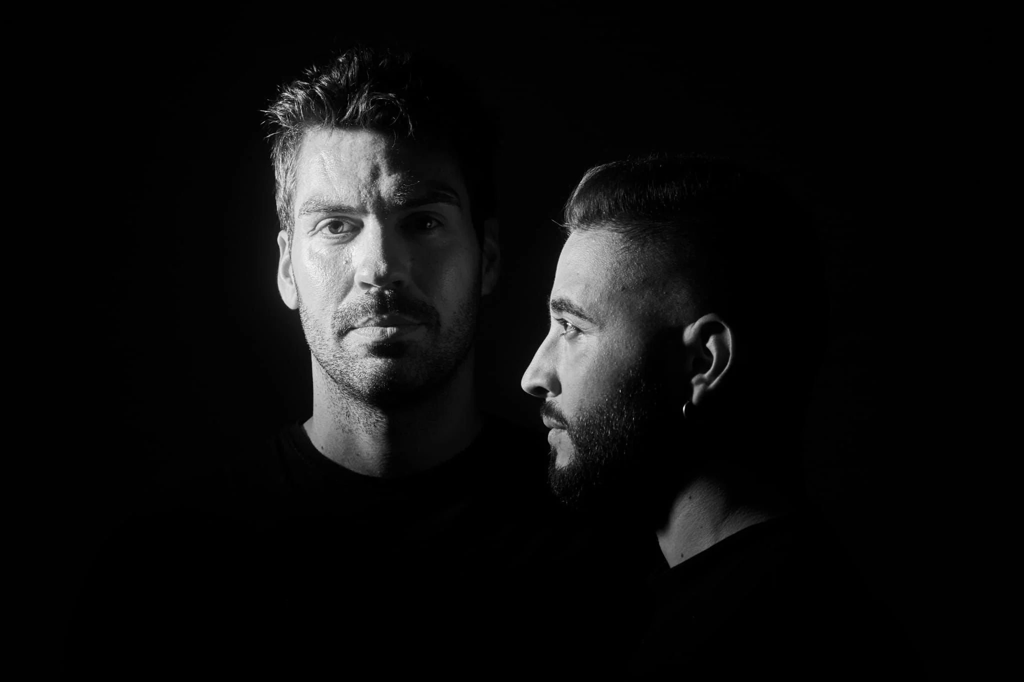 Retrato en blanco y negro de dos hombres con distinto perfil y expresión, uno de frente y otro de perfil, en un fondo oscuro.