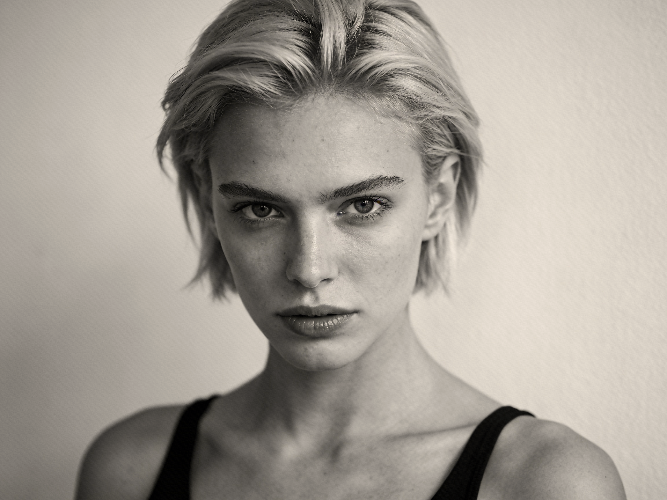 Schwarz-weiß Portraitaufnahme einer jungen Frau mit kurzen, blonden Haaren, die direkt in die Kamera schaut.