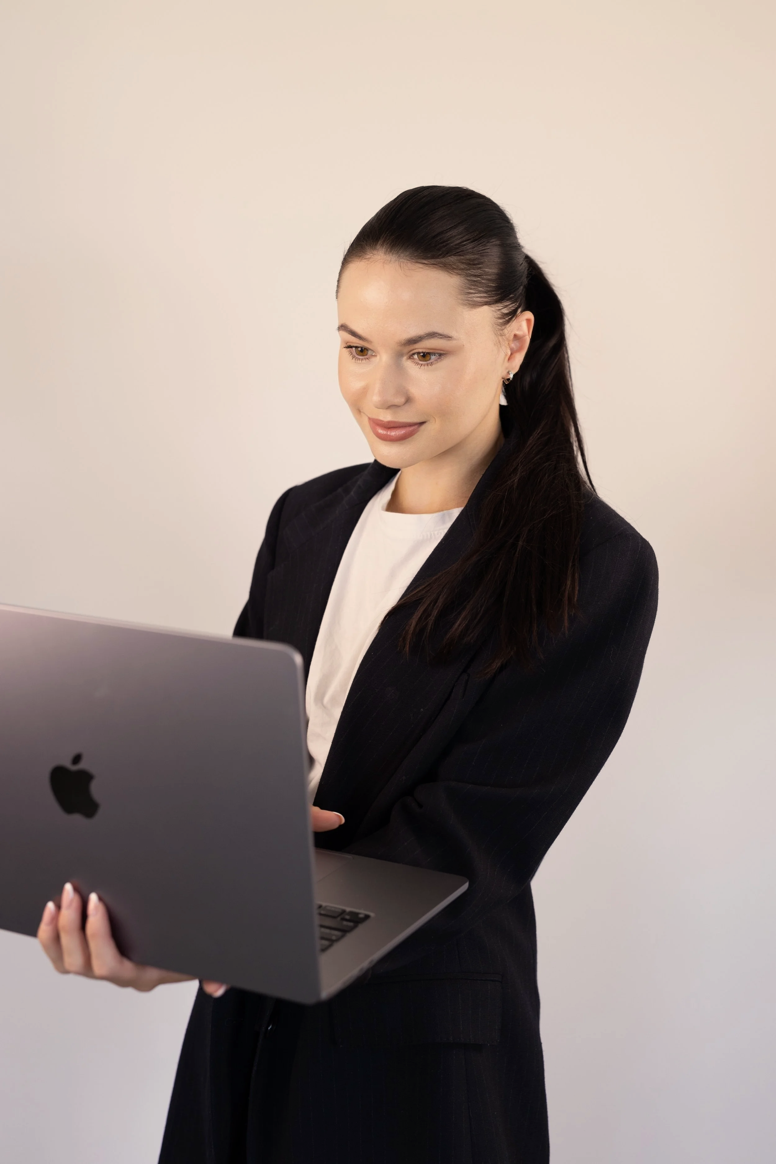 Junge Frau in Anzug mit schwarzen Haaren, die einen MacBook-Laptop hält und darauf schaut.