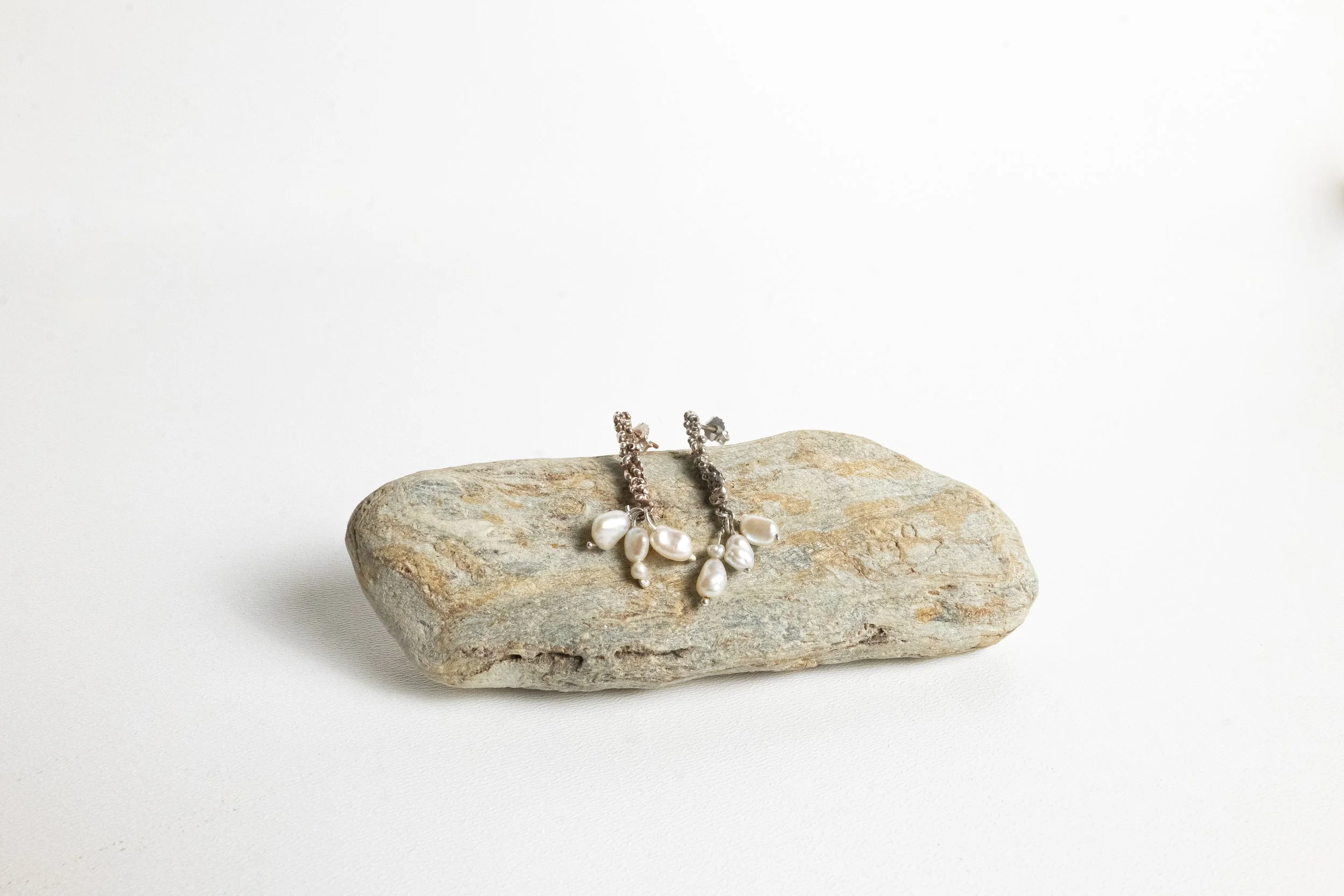 Pearl and gemstone earrings resting on a flat rock against a plain, light background.