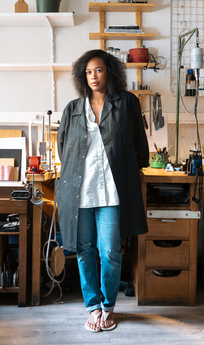 Femme debout dans un atelier avec des étagères en bois et des outils.