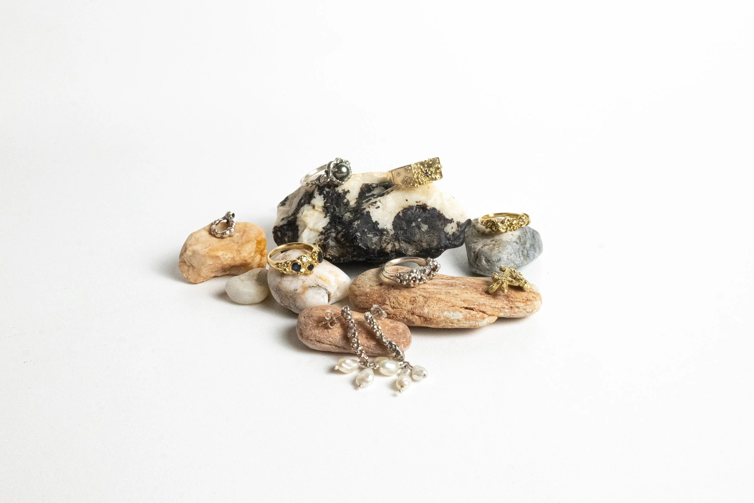 Jewelry, including rings and earrings, arranged on various small rocks on a white background.