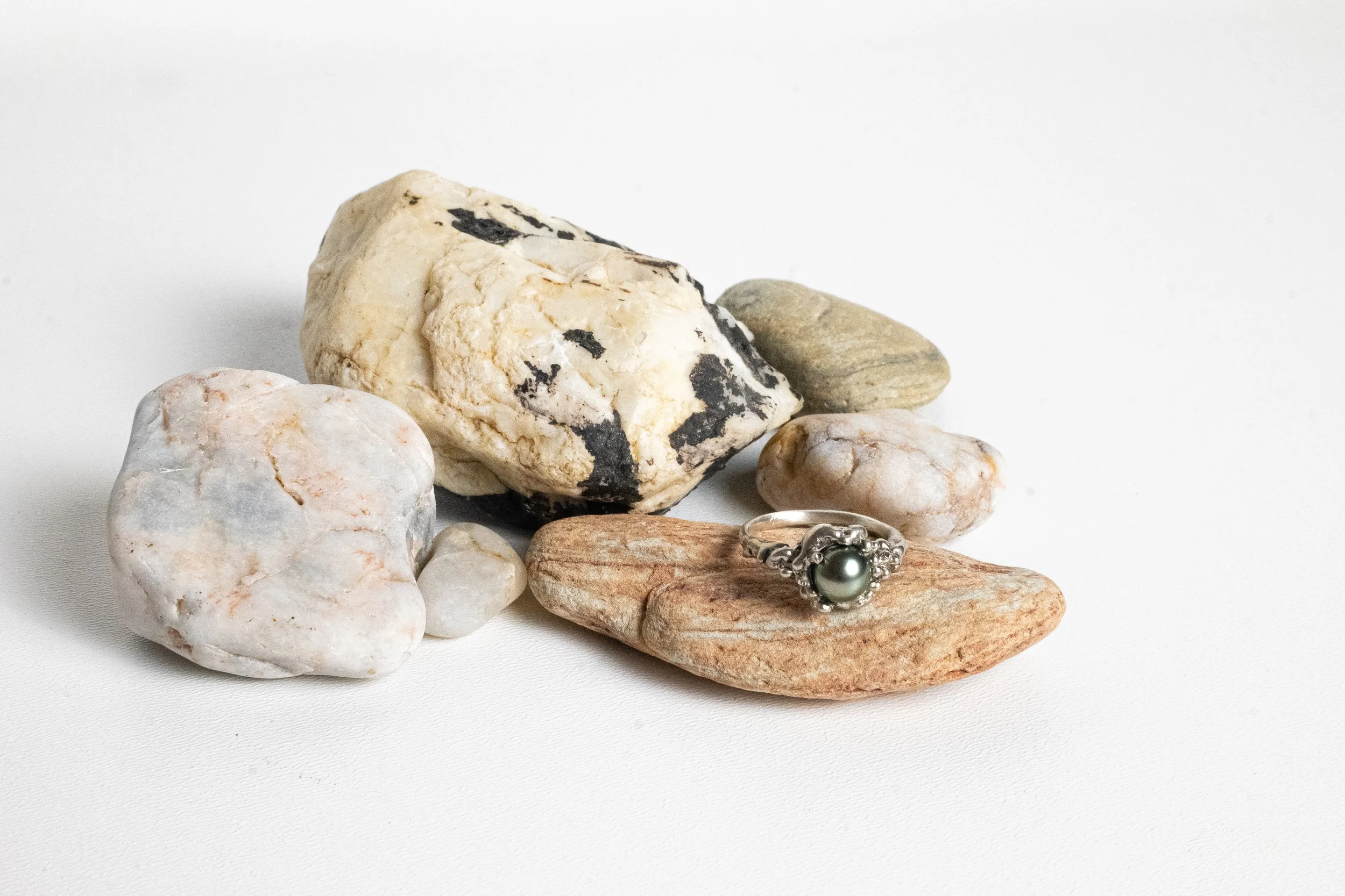 A collection of various rocks and a ring with a dark pearl on a white background.