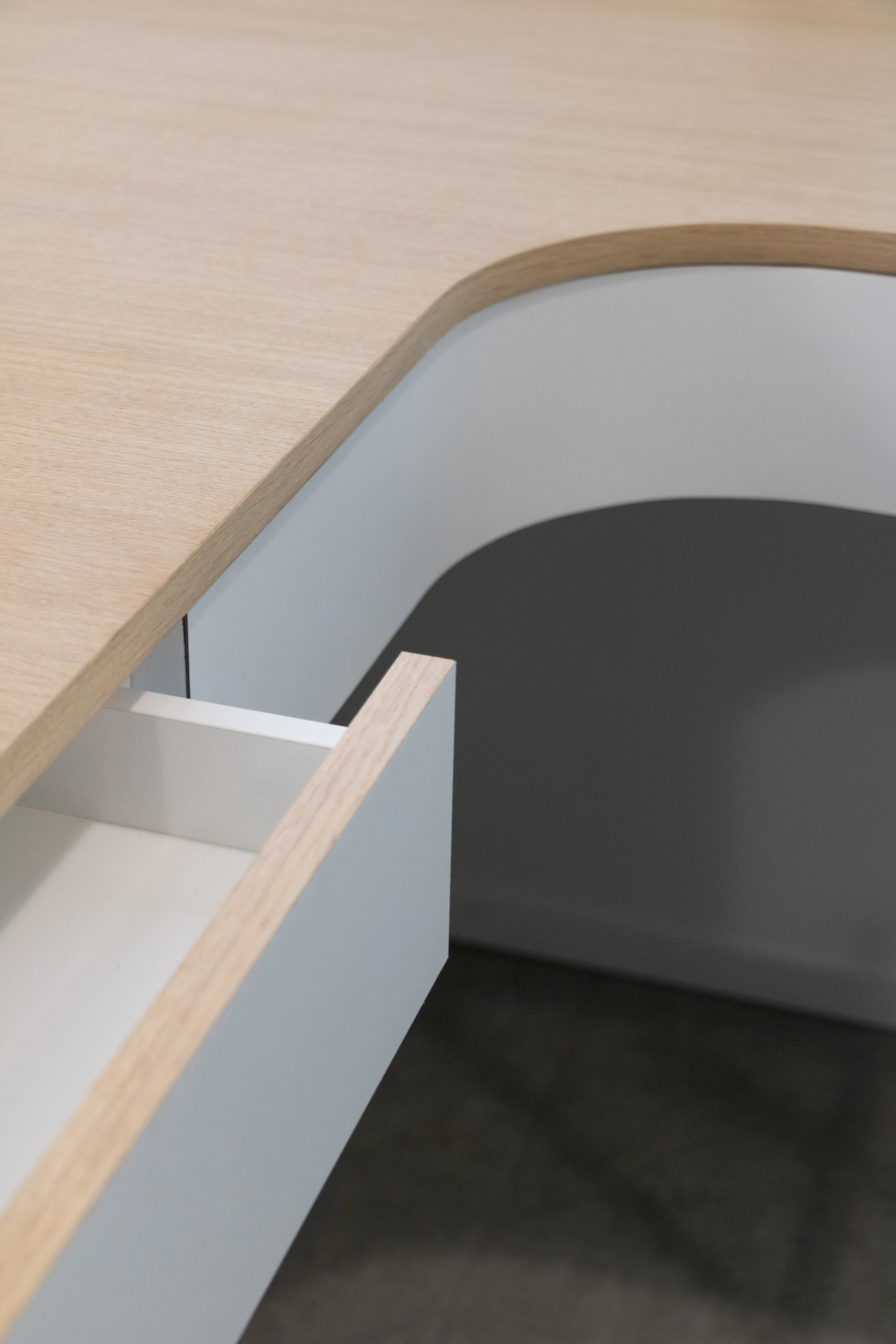 Close-up van een meubelstuk met een lichtblauwe lade en een houten bovenblad, met een boogvormige opening aan de achterkant.