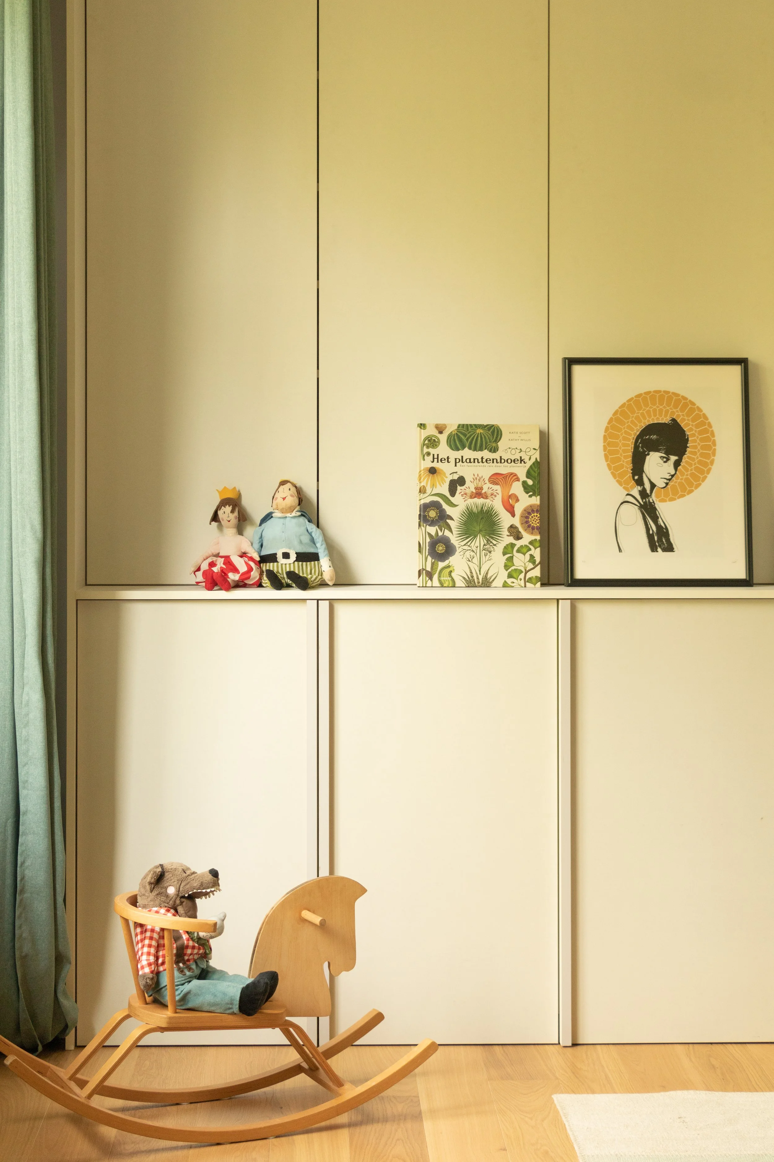 Woonkamer met een witte kast, speelgoedpoppen, een boek over planten, een schilderij van een meisje met een halo, en een houten schommel met een knuffelbeer.