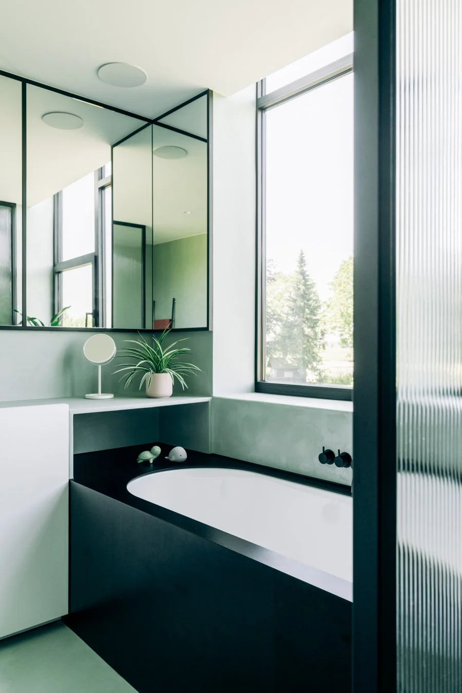 Moderne badkamer met een inbouwbad, grote ramen, een spiegelkast en planten.