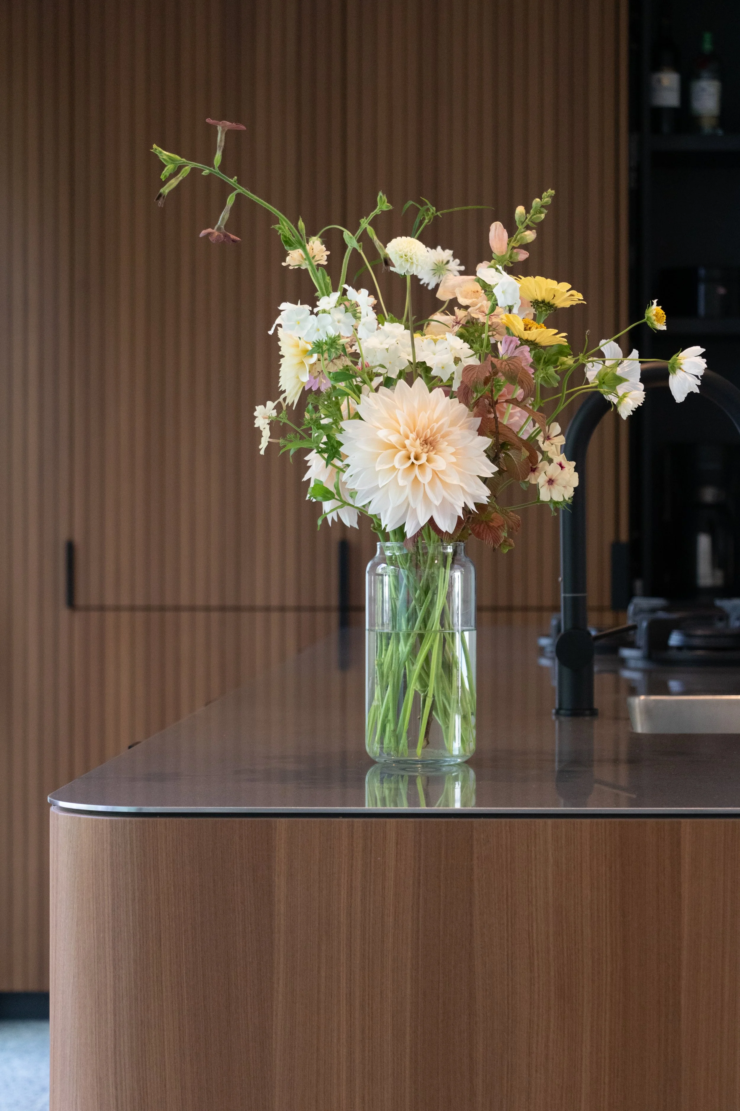 Een vaas met bloemen op een keukenaanrecht met een houten achterwand.
