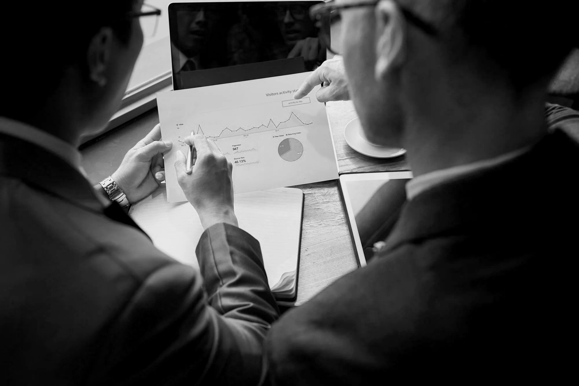 Two people examining a printed report with graphs and charts, one pointing at the paper, in a professional setting.