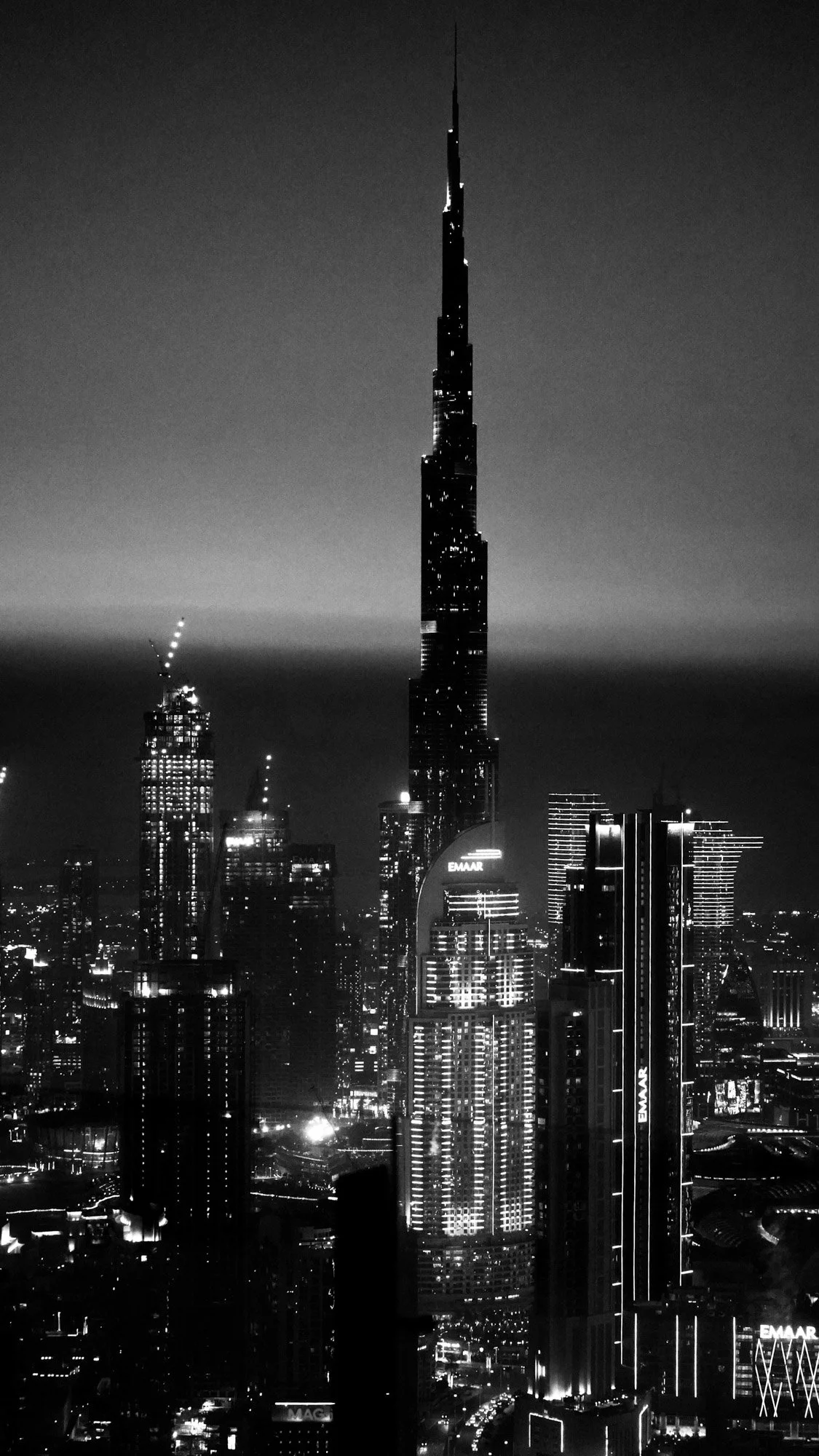 Night view of Dubai skyline featuring the Burj Khalifa illuminated among other skyscrapers with city lights.