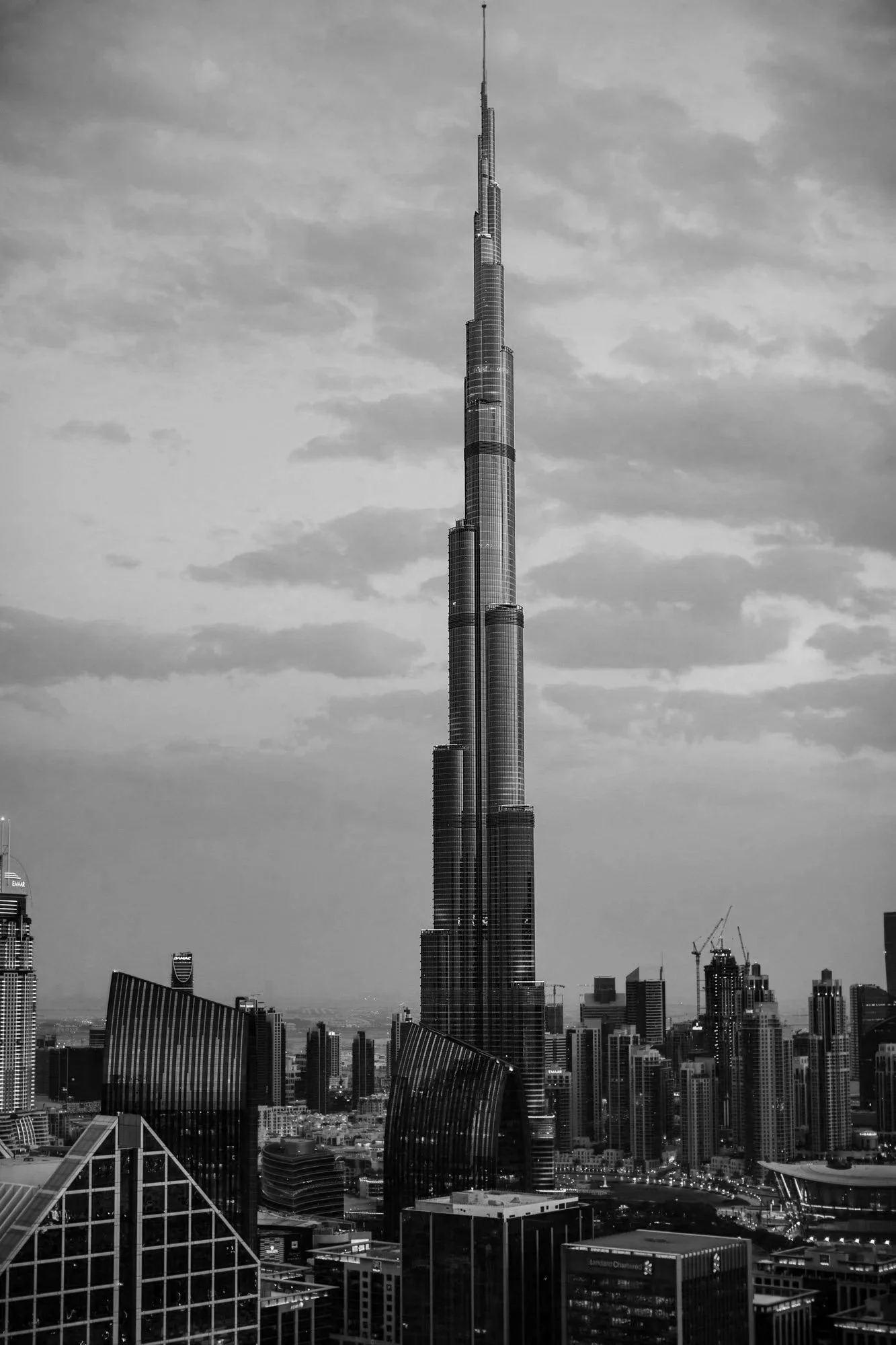 Black and white photo of the Burj Khalifa skyscraper in Dubai, towering over other modern buildings, with construction cranes visible in the city skyline.