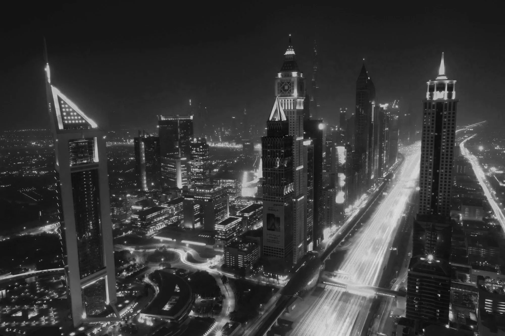 Nighttime cityscape featuring illuminated skyscrapers and highways in downtown Dubai, with motion blur from moving vehicles.