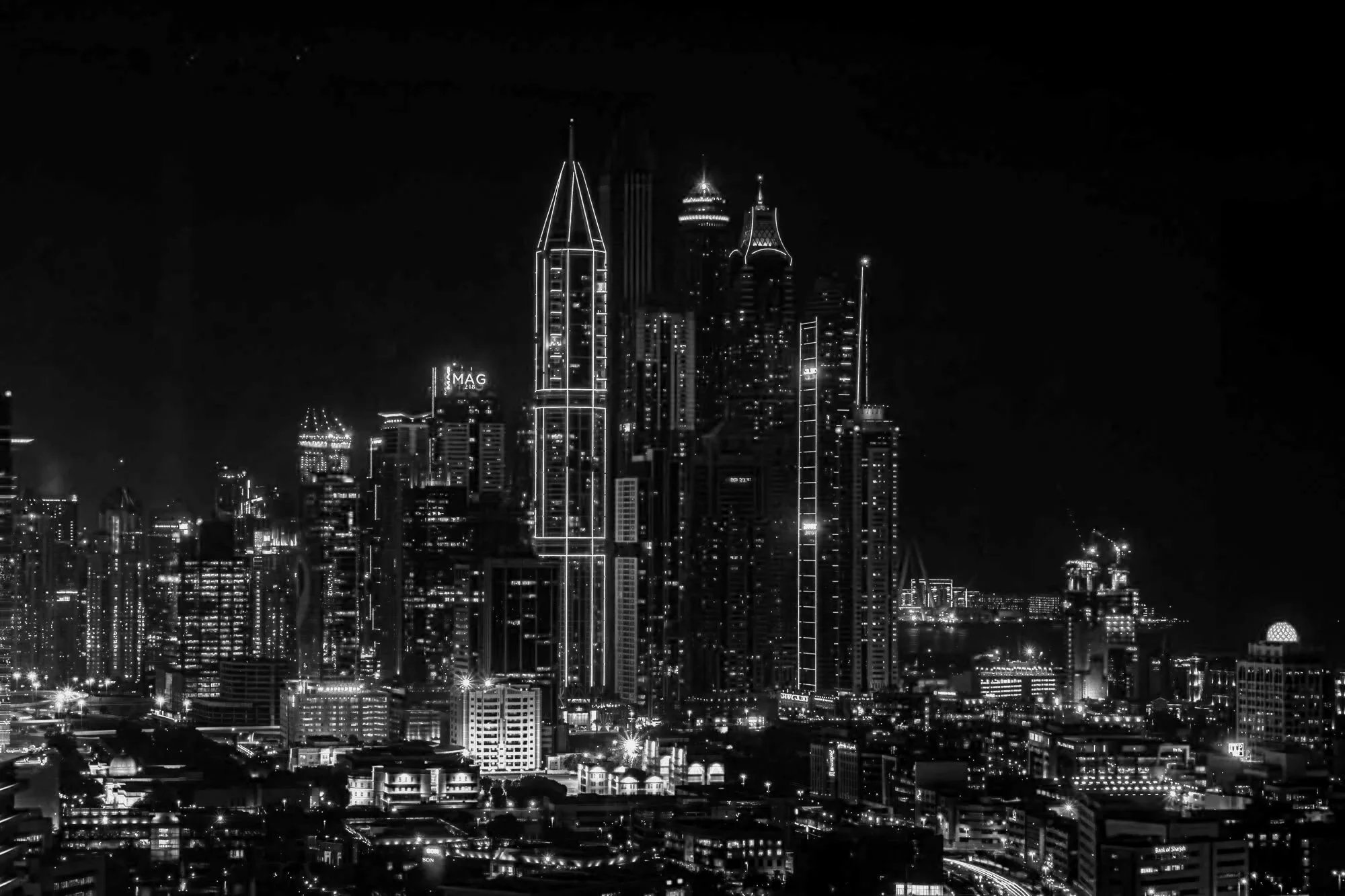 Night skyline of a city with illuminated tall skyscrapers, including distinctive designs, and a dark sky with no visible stars.